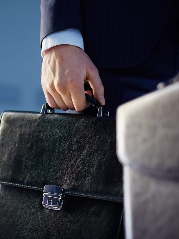 Cropped image of business partners carrying briefcases on the foreground while their colleague standing on the background